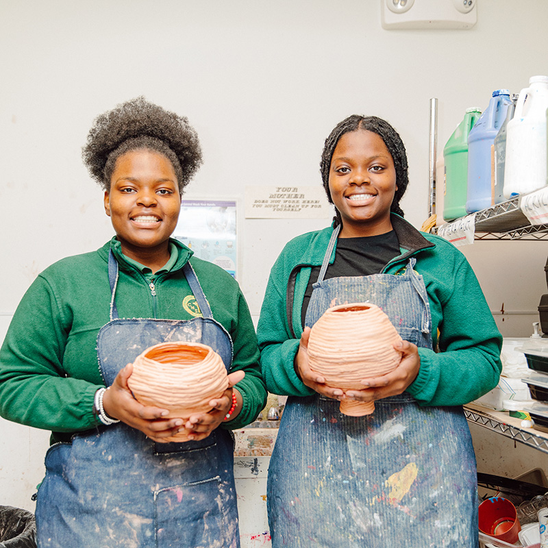 Two Cathedral scholars holding handmade pottery